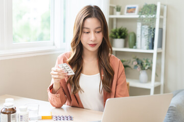 Wellness and dieting asian young woman, girl working from home using computer, typing or searching prescription on medicine label about vitamins information online, holding capsules of food supplement