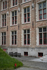 A brick building with multiple turrets and arched windows. The building has a medieval or renaissance style architecture. The building is surrounded by trees and shrubs. The sky is cloudy.