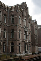 A brick building with multiple turrets and arched windows. The building has a medieval or renaissance style architecture. The building is surrounded by trees and shrubs. The sky is cloudy.