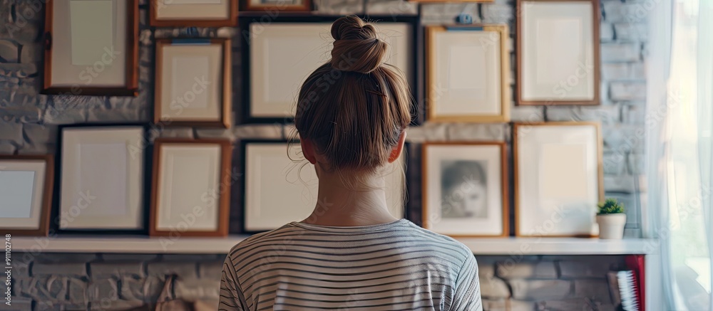 Wall mural back view of a young woman with empty picture frames displayed on a shelf at home creating a perfect