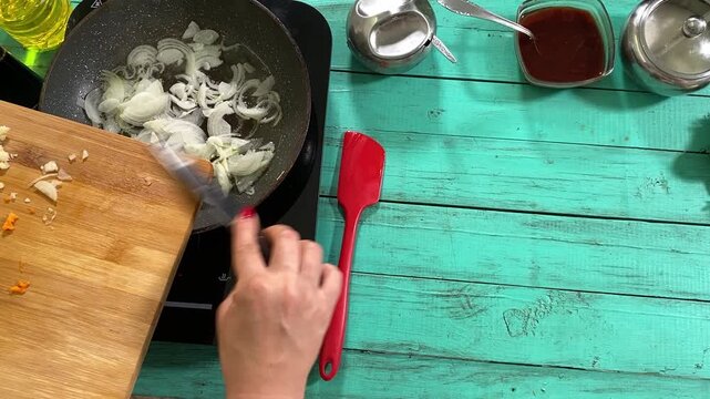 Culinary concept, preparation ingredients for homemade food. A young adult beautiful woman in an apron cooking a meal, makes mirepoix on a kitchen counter indoors. Home cooking and gastronomy passion