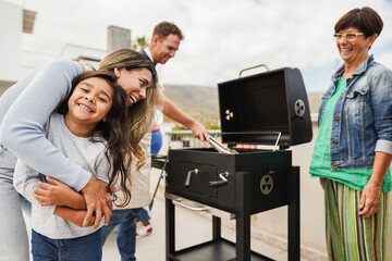 Family people doing barbecue at home's rooftop - Happy multiracial friends having fun eating and cooking together during weekend day - Summer and food concept - Main focus on kid face