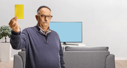 Serious mature man showing a yellow card in front of tv