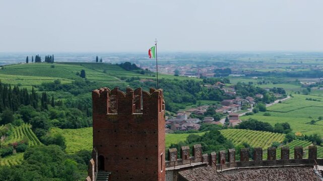 Aerial view of Soave castle tower with the Italian flag overlooking lush green countryside.