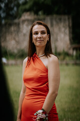Cesis, Latvia - July 12, 2024 - A woman in a red dress stands outdoors, wearing a pearl necklace...