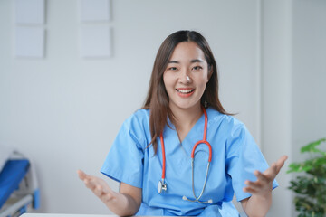 Friendly doctor is wearing blue scrubs and a stethoscope while sitting at a desk and talking to a patient online