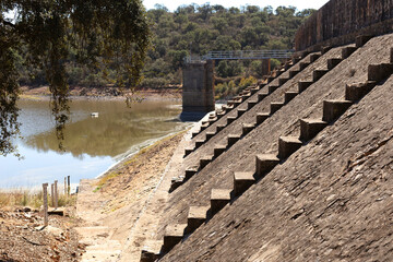 Fototapeta premium Wall of a reservoir gate, there are some stairs and a water depth marker. The water shortage due to drought is evident. Cornalvo Natural Park, Extremadura, Spain
