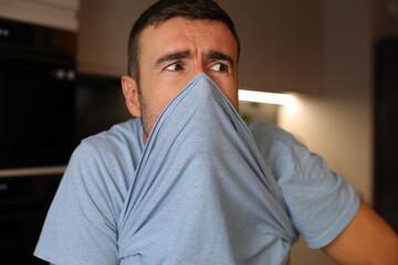 A stressed out man is blocking his nose with a t-shirt due to a bad scent