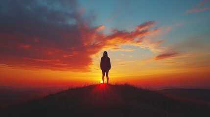 Obraz premium Silhouette of a person standing on a hill against a vibrant sunset, with dramatic colors and a serene atmosphere, emphasizing solitude and reflection