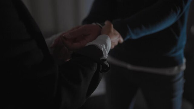 Policewoman handcuffing suspicious man indoors depicting law enforcement and arrest in a dimly lit room.