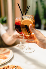 delicious pizzas are being enjoyed by two handsome people with cool cocktails on a beautiful white tablecloth in a cozy nice restaurant