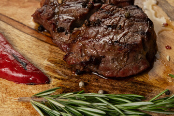 Closeup grilled Rib Eye Black Angus served with pepper and herbs on wooden background.