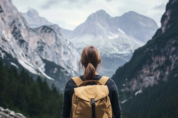 Fototapeta premium A rear view of a female traveller with a backpack facing beautiful mountains. 