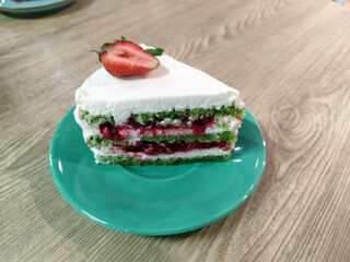 Dessert, sliced spinach cake with sour cream or cream cheese cream on a ceramic  green plate against the background of a wooden table. Dessert recipes. Turkish cuisine 