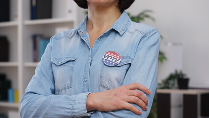 Serious woman with a vote pin standing at an election place, arms crossed on her chest