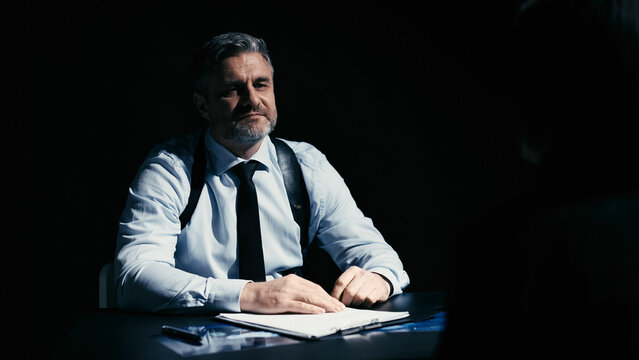 Self-confident police detective sitting with a smile, waiting for a confession from the suspect
