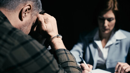 Female police detective questioning a man in handcuffs, suspect crying, confession