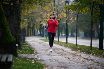 Obraz premium Young beautiful woman running in autumn park and listening to music with headphones on smartphone