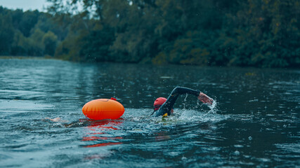 Triathlete in red swim cap and wetsuit powers through training session, perfecting stroke technique in preparation for swim leg of triathlon. Concept of sport competition, workout, recreation.