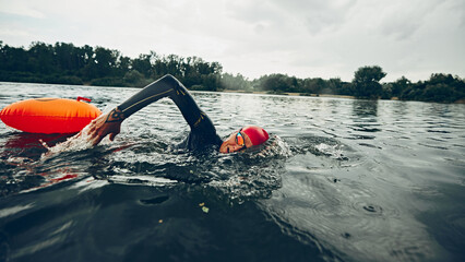 Triathlete in black wetsuit and red swim cap practices stroke, arm extended, water droplets flying,...