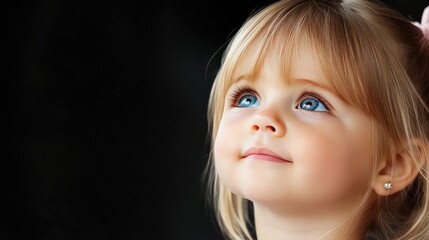 A toddler gazes upwards with wide, curious blue eyes, capturing the light in a dimly lit space, showcasing innocence and wonder