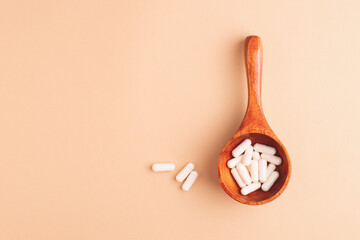 Wooden spoon with white capsules on beige background, top view. Dietary supplements and natural remedies in a simple, elegant composition.