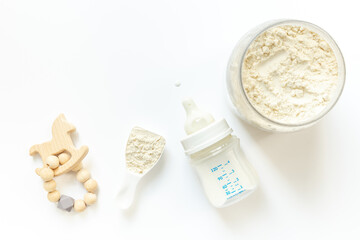 Milk for baby in a bottle with powdered milk in a spoon on white background, top view