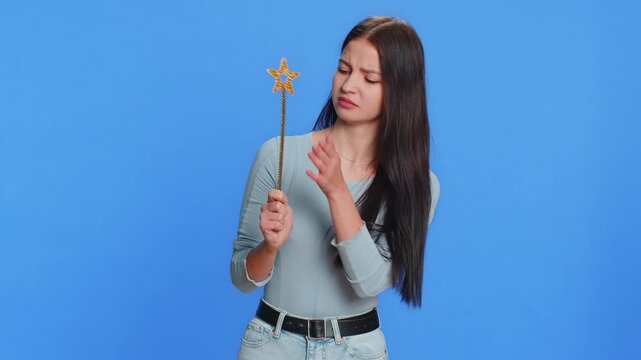 Magician witch young woman gesturing with magic wand fairy stick, making wish come true, casting magician spell, advertising holidays sale discount. Pretty girl isolated on blue studio background