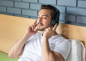 Happy man with headphones lying in bed enjoying music