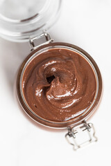 Chocolate butter, chocolate-nut paste in a glass jar on a light table, American breakfast