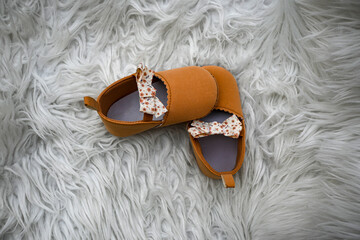 Pair of cute baby girl shoes with a bow is lying on white fur, waiting for the baby to wear