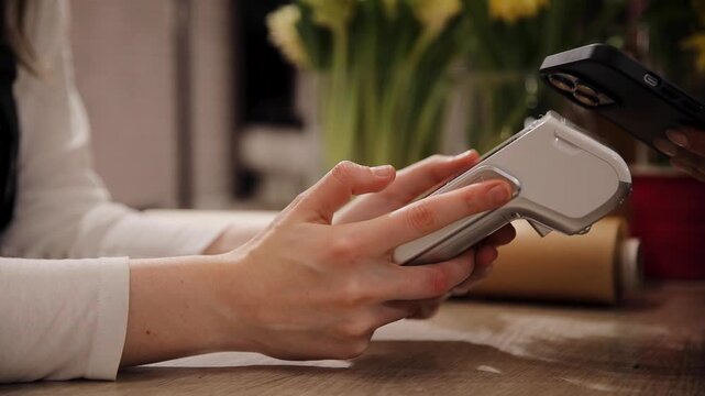 Close up of female florist selling bouquets of flowers holding payment terminal at beautiful cozy flower shop. Paypass or paywave wireless NFC technology