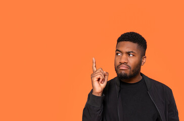 Man Pointing Upward Against a Vibrant Orange Background While Deep in Thought