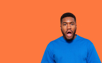 Surprised Young Man Expressing Shock Against Bright Orange Background in Casual Blue Attire