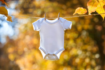 White baby onesie hanging on a clothesline outdoors in autumn with copy space, fall baby pregnancy announcement