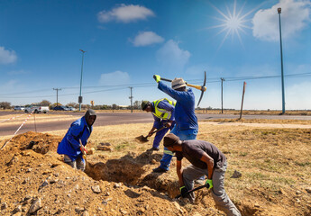 group of African workers digging a trench on the side of the highway installing optic fiber for...