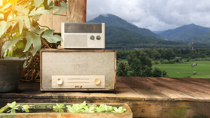 Image of almost rotten gray old fashion radio receivers on wooden planks floor with blur field and mountains view background.