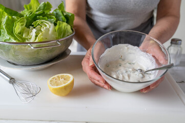 Woman preparing a healthy homemade salad dressing for green lettuce in the kitchen