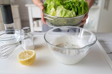 Woman preparing a healthy homemade salad dressing for green lettuce in the kitchen