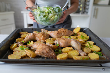 Homemade food, with oven roasted chicken legs and potatoes prepared by woman´s hands in the kitchen