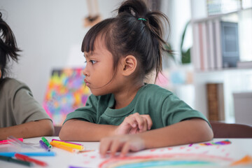 A young girl is sitting at a table with a pencil and a piece of paper in her hand. She is practicing drawing and coloring, honing her skills at home.