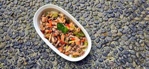 sauteed salty squid with black ink sauce with spicy seasoning called tumis cumi asin, is local Indonesian homemade cooking to include chili, ginger, and lime leaf served in a bowl