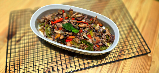 sauteed salty squid with black ink sauce with spicy seasoning called tumis cumi asin, is local Indonesian homemade cooking to include chili, ginger, and lime leaf served in a bowl