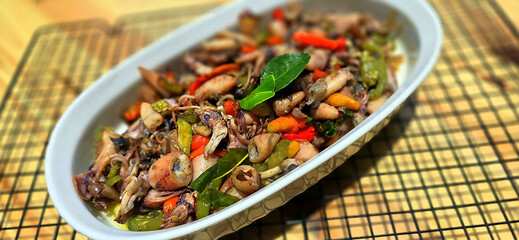 sauteed salty squid with black ink sauce with spicy seasoning called tumis cumi asin, is local Indonesian homemade cooking to include chili, ginger, and lime leaf served in a bowl