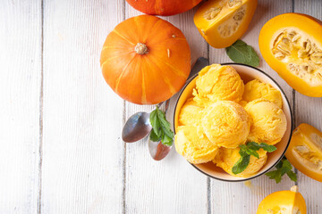 Pumpkin ice cream bowl. Tasty pumpkin squash gelato scoops in portioned bowl, on wooden table with sliced pumpkin squash, copy space