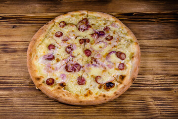 Pizza with sausages, ham and parmesan cheese on a wooden table