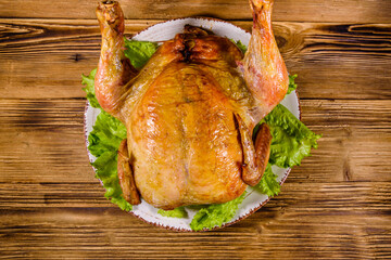 Plate with roasted whole chicken and lettuce leaves on a wooden table. Top view