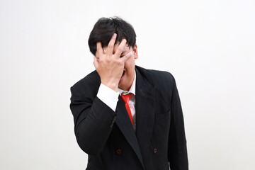 Deeply disappointed and shocked asian businessman in suit making face palm. Isolated on white
