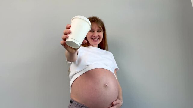 Happy young pregnant woman is drinking coffee or tea from paper cup