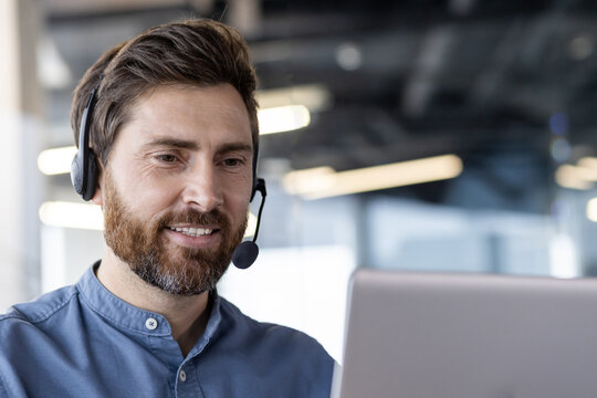 Smiling businessman with headset working on laptop in modern office setting